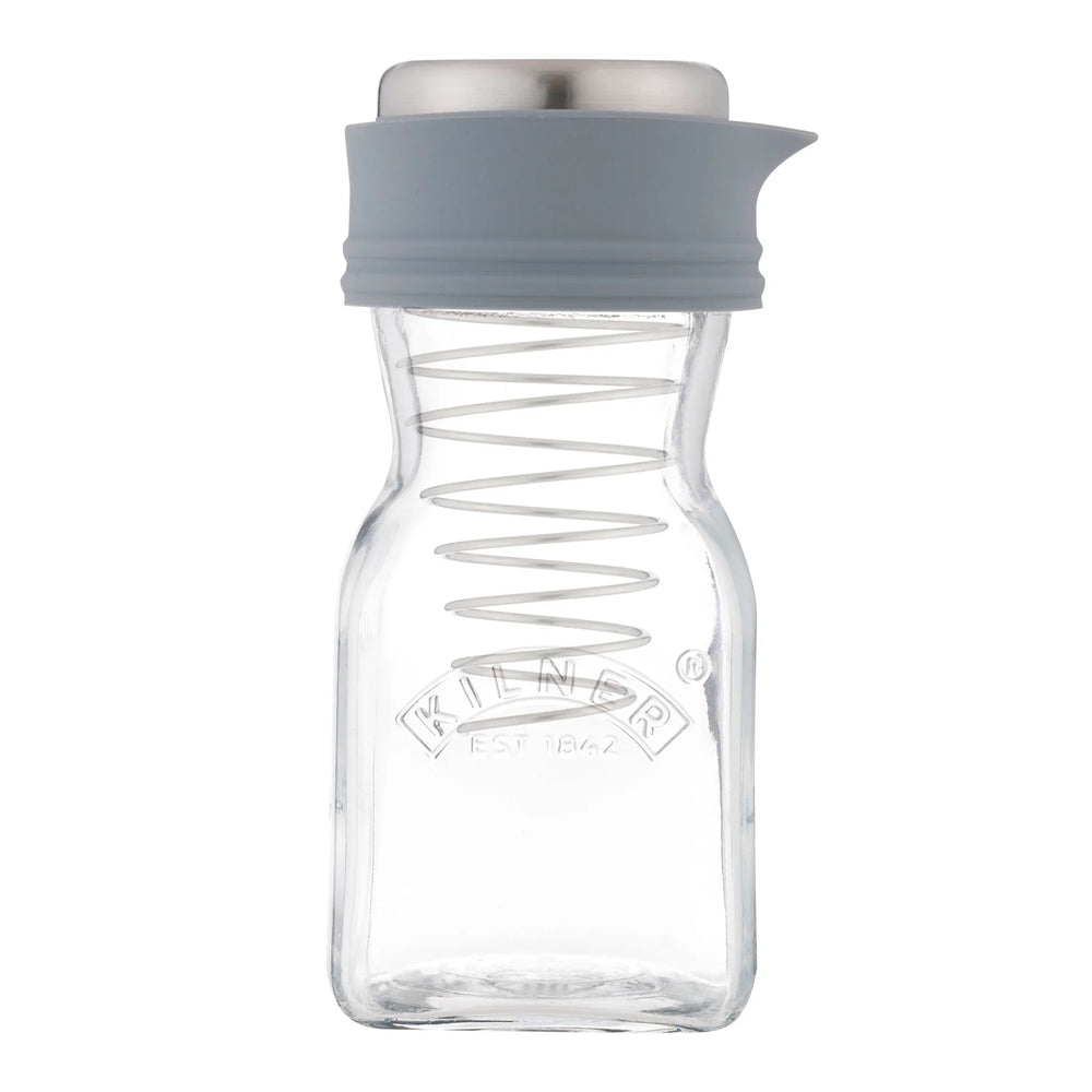 A clear glass spice jar with a grey silicone pour spout and lid, featuring a metal spring inside and the Kilder brand logo embossed on the front, set against a plain white background.