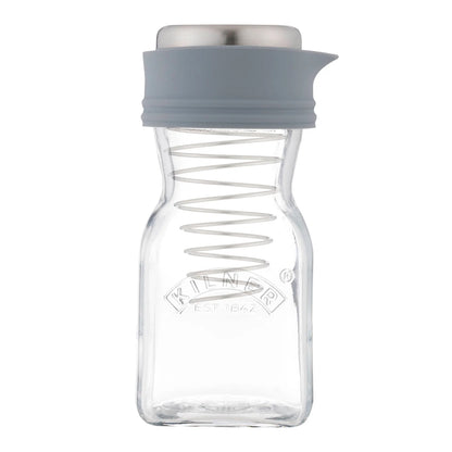 A clear glass spice jar with a grey silicone pour spout and lid, featuring a metal spring inside and the Kilder brand logo embossed on the front, set against a plain white background.