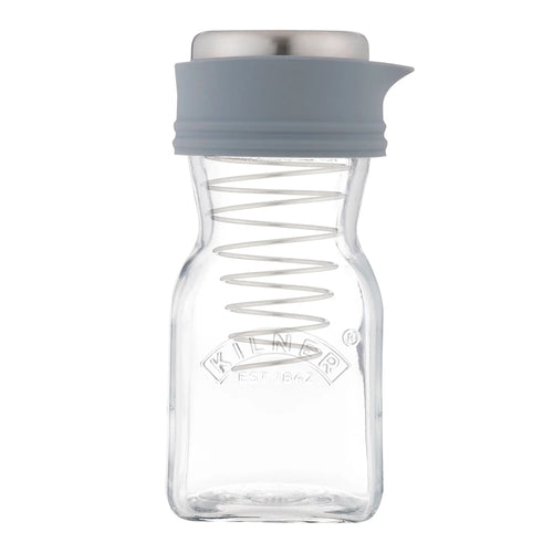 A clear glass spice jar with a grey silicone pour spout and lid, featuring a metal spring inside and the Kilder brand logo embossed on the front, set against a plain white background.