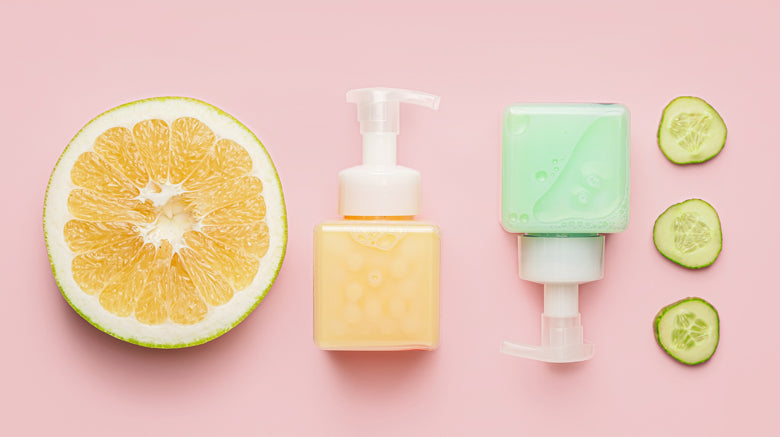 Bottles of liquid soap on a pink background with slices of fruit