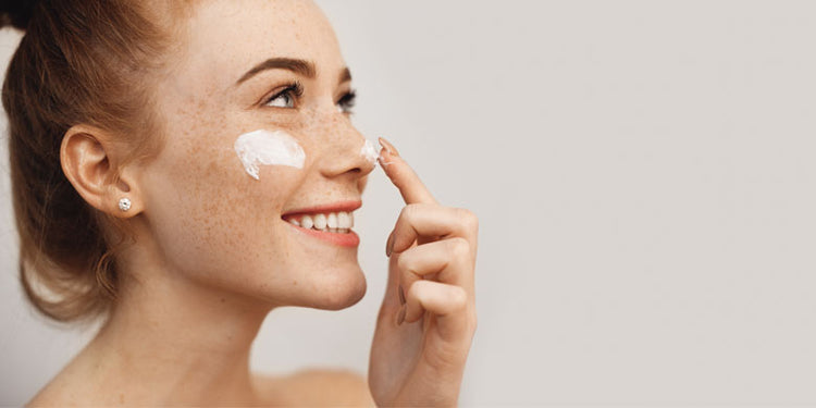 smiling girl applying moisturiser to her face
