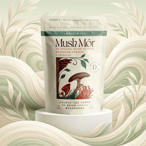 A stand-up pouch of Mush Mór mushroom powders and extracts centered on a white pedestal, with a decorative illustrated label showing mushrooms and botanical elements. The background is a soft, stylized cream and sage abstract floral pattern.