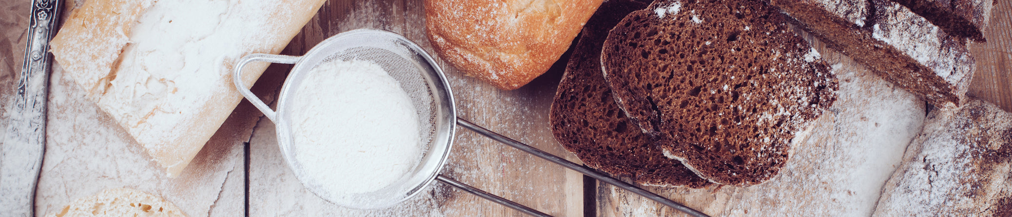 A rustic flat-lay of various breads and a metal bowl of flour on a wooden surface, with a large blurred square overlay covering the center. Irish Food & Drink

