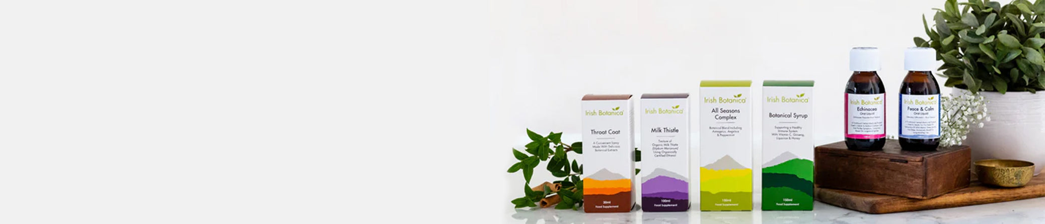 A horizontal banner featuring Irish Botanica supplement products, arranged on a white background with small green plants and a wooden tray.