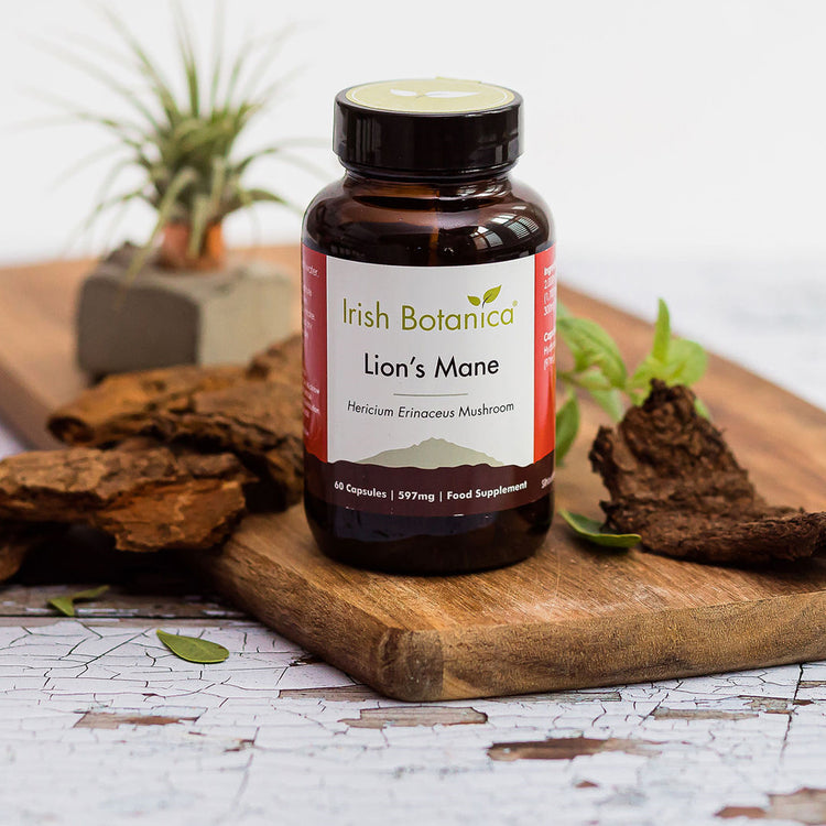 Irish Botanica Lion's Mane stands on a wooden cutting board with dried mushroom slices and green leaves around it.