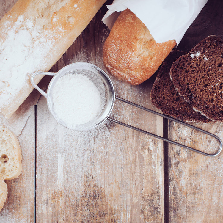 A rustic flat-lay of various breads and a metal bowl of flour on a wooden surface, with a large blurred square overlay covering the center. Irish Food & Drink