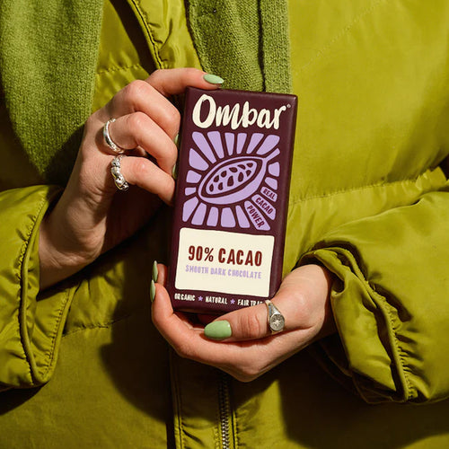 Person holding an Ombar 90% Cacao chocolate bar against a green jacket.