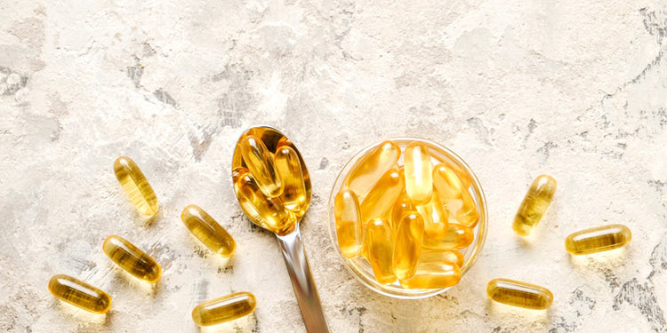 Oil supplement capsules on spoon and in jar on marble surface
