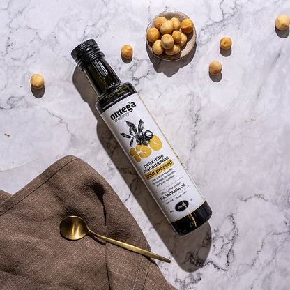 Bottle of Omega Macadamia Oil on a marble surface with macadamias and a spoon.
