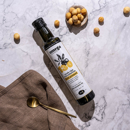 Bottle of Omega Macadamia Oil on a marble surface with macadamias and a spoon.