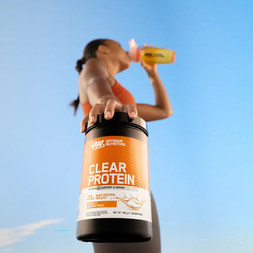 Person holding a container of Optimum Nutrition Clear Protein against a blue sky.