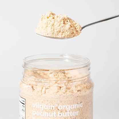 A clear jar of Vilgain Organic Peanut Butter with a spoonful of the beige powder 