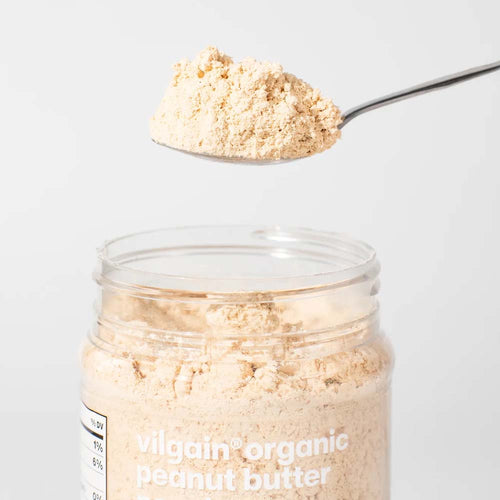 A clear jar of Vilgain Organic Peanut Butter with a spoonful of the beige powder 