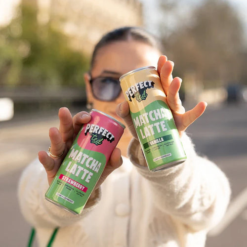 Person holding two cans of Perfect Matcha Latte in different flavors.