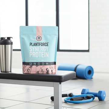 Plantforce Synergy Protein powder pouch displayed on a gym bench in a bright gym setting.