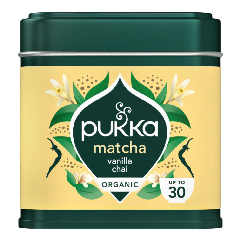 A tin of Pukka Matcha Vanilla Chai organic tea, featuring a dark green metal container with a pale yellow label decorated with green leaves, white flowers, and black silhouettes.