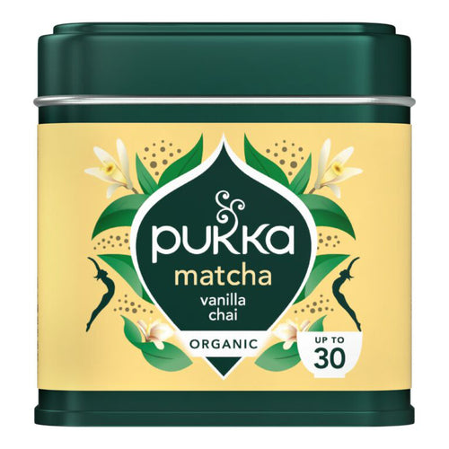 A tin of Pukka Matcha Vanilla Chai organic tea, featuring a dark green metal container with a pale yellow label decorated with green leaves, white flowers, and black silhouettes.