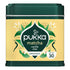 A tin of Pukka Matcha Vanilla Chai organic tea, featuring a dark green metal container with a pale yellow label decorated with green leaves, white flowers, and black silhouettes.