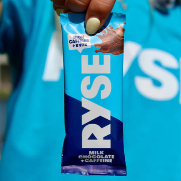 Ryse milk chocolate with caffeine package held by a hand against a blurred blue background
