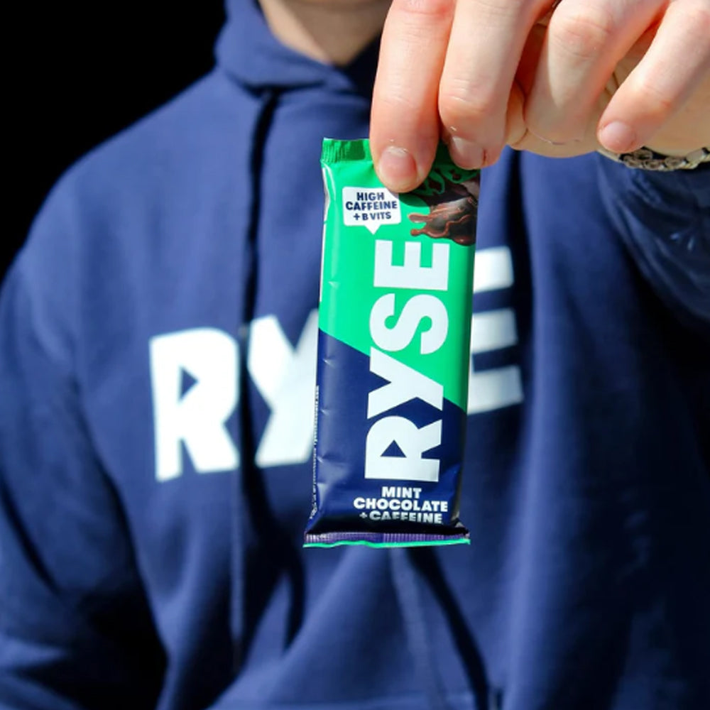 Person holding a RYSE mint chocolate caffeine bar in front of a blue hoodie