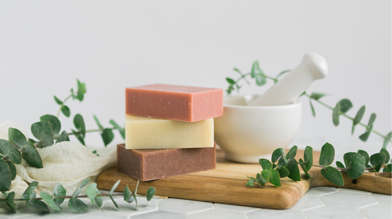 bars of handmade soap on a wooden cutting board with pestle and mortar