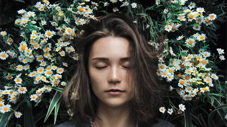 woman with eyes closed lying in daisies