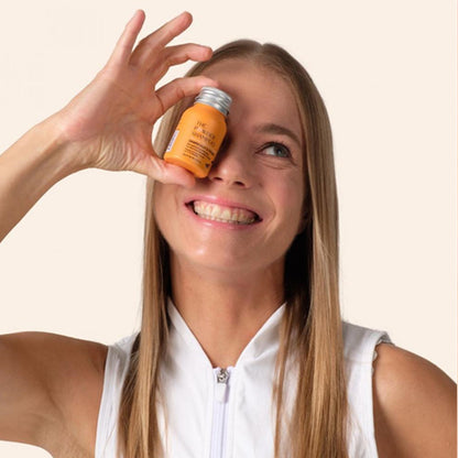 Woman holding a small jar to her eye against a plain background