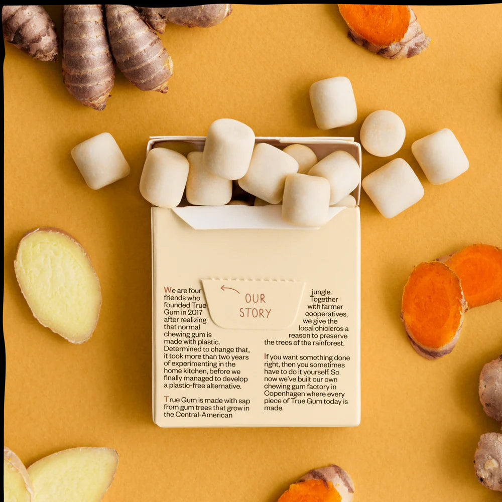 Open container of True Gum with marshmallows on a yellow background with turmeric roots.