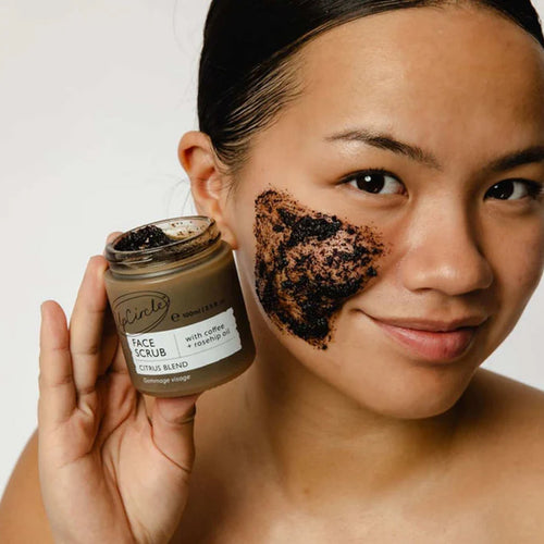 Woman applying coffee face scrub with a jar of the product.