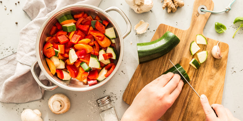 pot of fresh vegetables with hands chopping a courgette