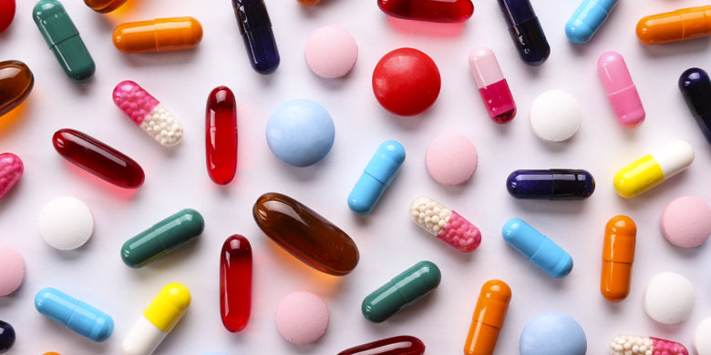 range of colourful capsules and tablets on pink background