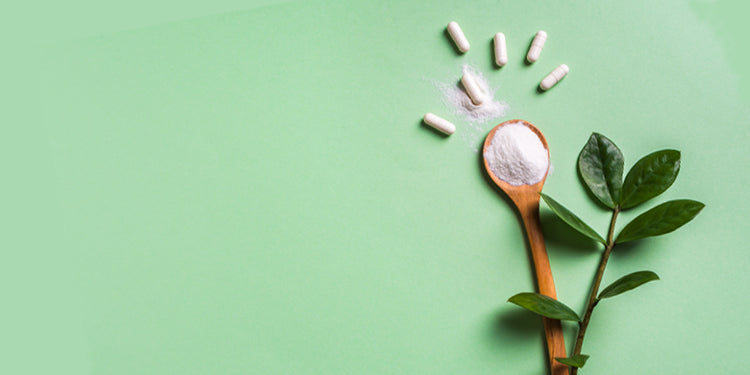 Wooden spoon with white powder and capsules on green background