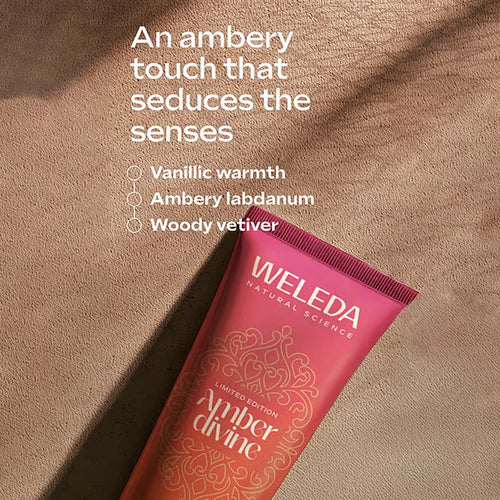 A squeeze tube of Weleda Amber Divine lotion lies diagonally on a textured tan surface with soft shadows. White text above describes the scent as having an ambry touch with vanillic warmth, ambry labdanum, and woody vetiver.