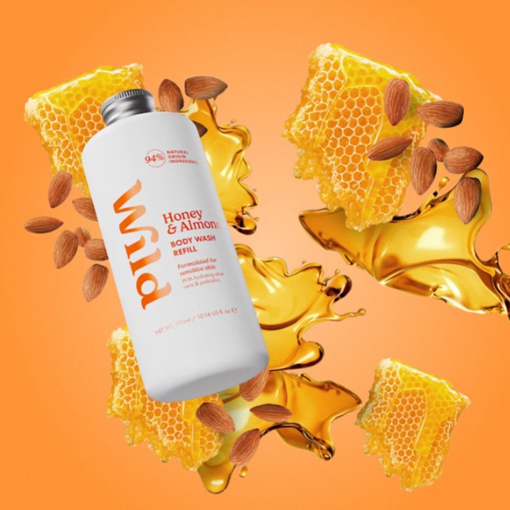 A white bottle of Wild Honey &amp; Almond Body Wash Supernova floating over a stylized orange background with honeycomb, almonds, and golden honey splashes. 