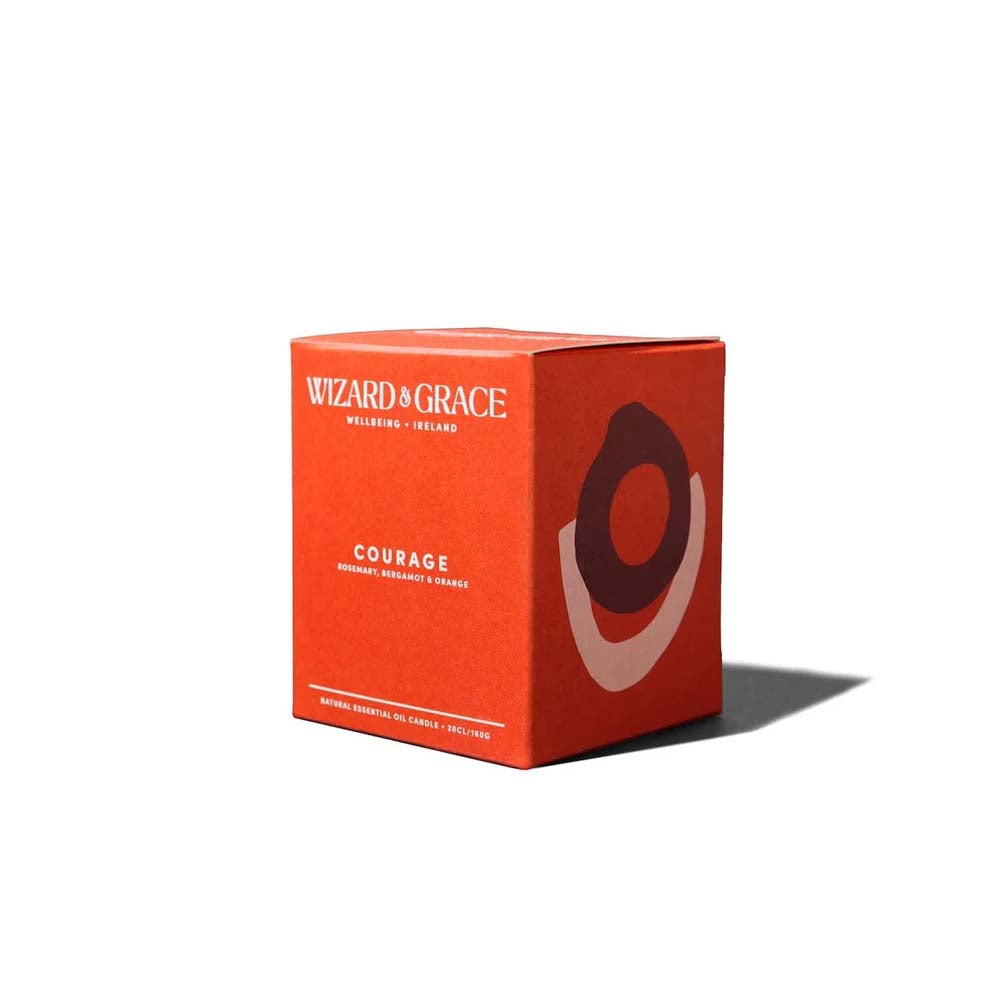 A bright orange square packaging box for the Wizard &amp; Grace Courage natural essential oil candle, featuring abstract layered oval artwork on the side.