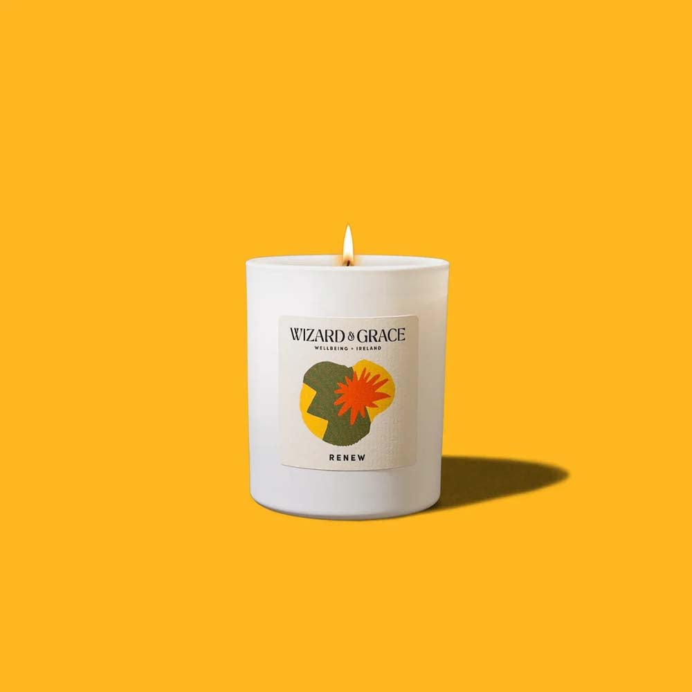 Lit Wizard &amp; Grace "RENEW" natural candle in a white jar set against a vibrant yellow background.