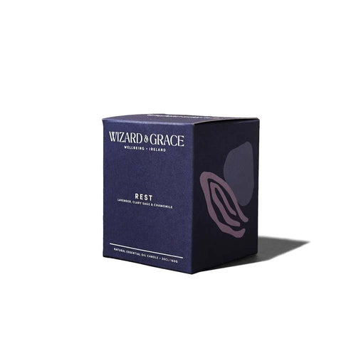 Dark navy blue packaging box for the Wizard & Grace "REST" natural essential oil candle, featuring abstract purple botanical illustrations on a clean white background.