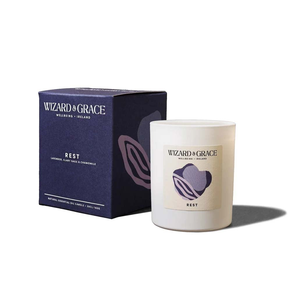 Wizard &amp; Grace "REST" natural essential oil candle in a matte white jar next to its dark navy blue packaging box, scented with lavender, clary sage, and chamomile.