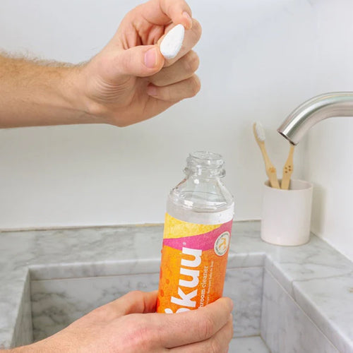 Person holding a bottle of Iskku water over a sink.
